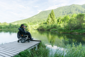 Disabled person on wheelchair photographing at lake in nature