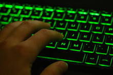 Man's Hand Typing On Keyboard With Green Backlight