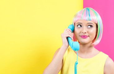 Wall Mural - Young woman in a colorful wig talking on a retro phone on a split yellow and pink background