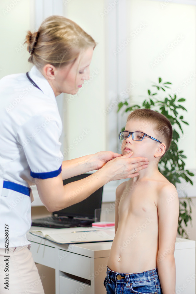 Chłopiec w okularach badania lekarskiego. Lekarka w gabinecie lekarskim podczas badania migdałków u chłopca w okularach - obrazy, fototapety, plakaty 