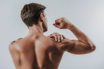 close up of muscular man touching shoulder and banding elbow