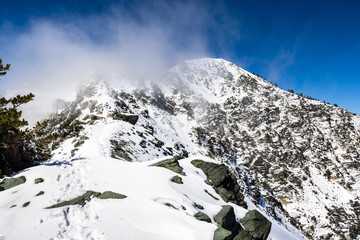 Rocky ridge on the trail towards the top of Mount San Antonio (Mt Baldy) on a snowy but sunny day, with fog rising from the valley, Los Angeles county, south California