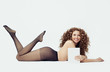 Pretty woman wearing black tights lying on white background and showing empty paper card