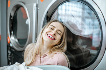 Wall Mural - Young and cheerful woman enjoying the washing process standing near professional drying machine in the laundry