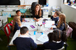 © Monkey Business - Elevated view of female primary school teacher sitting at a table smiling in a classroom with schoolchildren during a lesson