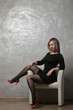 © MK studio - Beautiful girl with red lips and in a black dress sitting in a chair against the background of a gray concrete wall. emotion. different poses