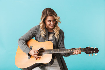 Wall Mural - Smiling young girl playing a guitar while sitting isolated