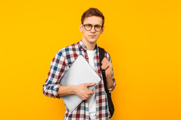 Happy guy with glasses, a man in a plaid shirt, with a closed laptop in hand, on a yellow background