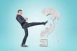 © gearstd - Side view of man in suit kicking and smashing a big stone question mark.