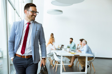 Young businessman leaves a meeting while other people stay in office