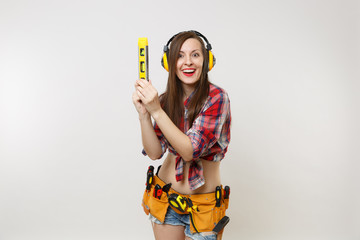 Wall Mural - Pretty handyman woman in plaid shirt, denim shorts, noise insulated headphones, kit tools belt full of instruments hold building bubble spirit level isolated on white background. Female in male work