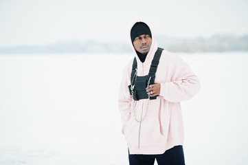 Wall Mural - Stylish urban style african american man in pink hoodie posed at frozen lake in winter.