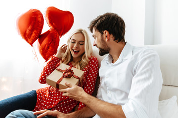 Wall Mural - Couple. Love. Valentine's day. Emotions. Man is giving a gift box to his woman, both smiling; at home