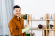 © LIGHTFIELD STUDIOS - handsome man standing in modern living room and holding bottle while smiling at camera