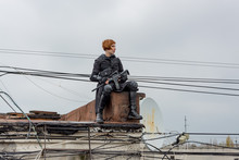 Young Woman In Modern Black Techwear Style With Rifle Posing On The Rooftop, Portrait Of Redhead Woman Cyperpunk Or   Post Apocalyptic Concept