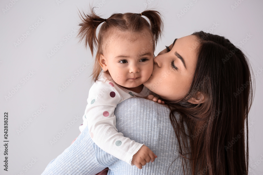 Young mother with her cute little daughter on light background
