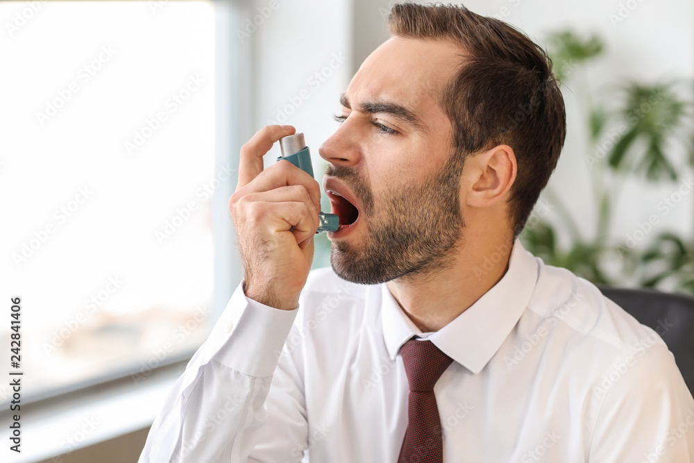 Young man with inhaler having asthma attack in office