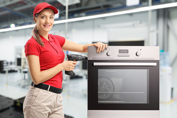 Poster - Repairwoman with a drill and oven at a factory looking at the cameraand smiling