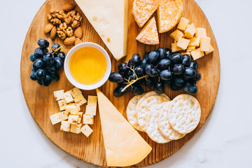 Wall Mural - Flat lay with various types of cheese, grapes, nuts, honey and cracker in wooden board on marble