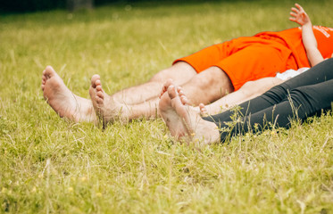 Canvas Print - Happy family lying on green grass. family feet closeup