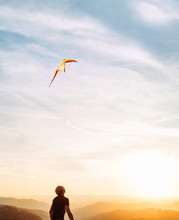 Man Starting To Fly Bright Kite In Sunset Sky Over The Mountain. Successful Startup Concept Image.
