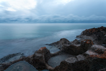 Seascape of coastline in Puglia at sunset during the blue hour with rocks in foreground and stormy clouds in background