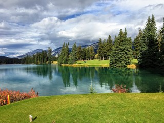 A nice view of a difficult par 4 on a golf course that demands your first drive off the tee carry a large lake in order to hit the fairway.  The golf hole is by a lake with mountain a nice background