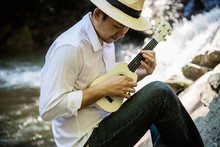 Man Play Ukulele New To The Waterfall - People And Music Instrument Life Style In Nature Concept