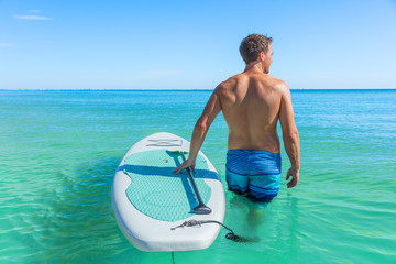 Stand up paddle boarding fitness man swimming in turquoise caribbean ocean water.