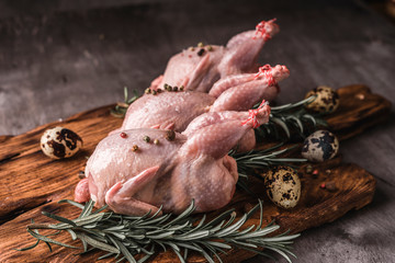 Raw meat of quails, rosemary, pepper and vegetables on the kitchen table.