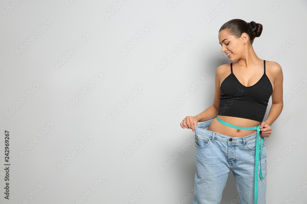 Slim woman in oversized jeans with measuring tape on light background, space for text. Weight loss - obrazy, fototapety, plakaty 