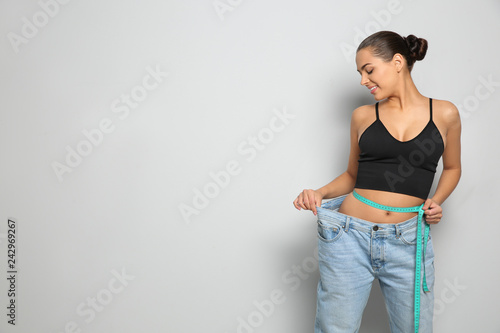 Cuadros en Lienzo Slim woman in oversized jeans with measuring tape on light background, space for text