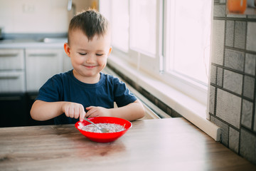 A child in the kitchen eating their own oatmeal with a red plate