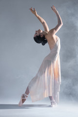 Elegant woman female girl ballerina dancer in beige dress dancing, making emotional performance and dance element in fog dust smoke fume on isolated grey background scene. Dancing in cloud concept