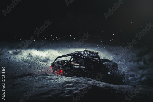 Obraz Dibond Sterowany radiowo samochód na śniegu w nocy, świecą światła. Świąteczna rozrywka prezent rc car