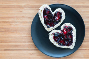 Heart shaped toasts on a plate over wooden background, top view