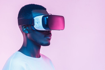 VR concept. Young african man wearing  virtual reality goggles, isolated on pink background