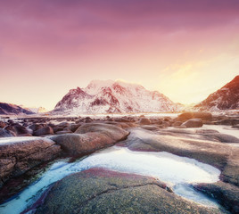 Wall Mural - Mountains, stone, water and sunrise on Lofoten islands, Norway. Natural landscape in the Norway. Sunrise on the seashore and reflection on the water surface