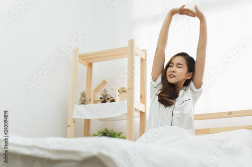 Fotografie, Obraz Asian woman wake up in the morning, sitting on white bed and stretching, feeling
