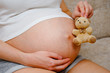 © gesrey - A pregnant girl in a t-shirt is holding a teddy bear toy.