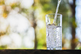 Fototapeta Łazienka - closeup Pouring fresh water on drinking glass over nature sunlight morning background