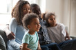 © fizkes - Happy black family with children sitting on couch watching tv together, african american parents embrace kids relaxing on sofa laughing enjoying funny cartoons or movie having fun on weekend at home