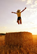 Girl jumping on a straw bale at sunset.