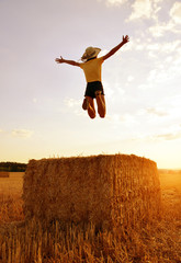 Girl jumping on a straw bale at sunset.