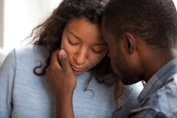 Loving african american husband apologizing comforting sad wife, caring man consoling gently touching face of upset woman, compassion, empathy and support in black couple relationships concept