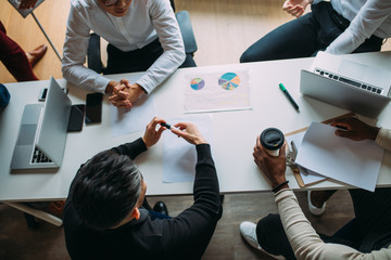 Wall Mural - Top view of multiracial creative business men in white and black formal clothes disputing at a meeting using gadgets during the conference while sitting at the modern office.