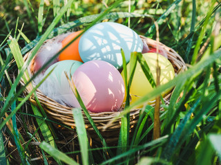 Basket with colorful Easter eggs standing on the green grass against the bright rays of the spring sun. Happy Easter. Preparation for the holiday