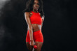 © Mike Orlov - Sporty fit black skin woman in red sportswear, athlete with dumbbells makes fitness exercising on dark background.