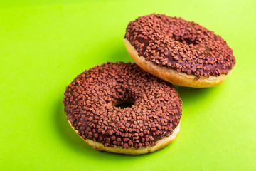 Two delicious chocolate donuts with sprinkle on bright green background