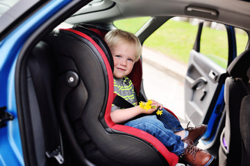 portrait of a young child of a boy with blond hair in a children's car seat. Safe transportation of children in the car.